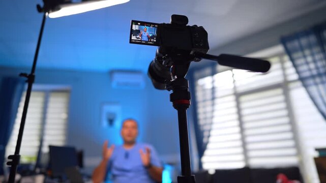 Camera on a tripod taking video of a talking man in blue uniform. Low angle view. Modern vlogging concept. Selective focus.