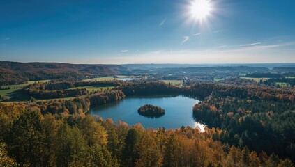 Bird's-eye view of a reservoir surrounded by meadows and vibrant fall woods in a mountainous region