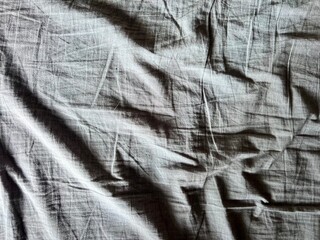 a wrinkled gray bed sheet with a ray of sunlight woman hand