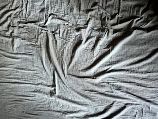 a wrinkled gray bed sheet with a ray of sunlight woman hand