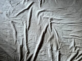 a wrinkled gray bed sheet with a ray of sunlight woman hand