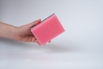 Obraz premium Hand holding pink cleaning sponge on white background. Household cleaning or hygiene concept, minimal style product photo. 