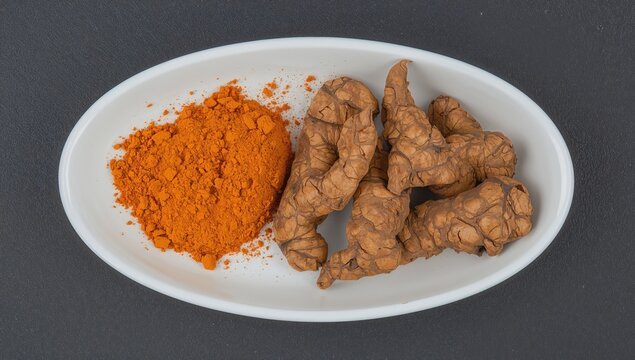 Ground turmeric and whole roots displayed on a white dish against a dark backdrop