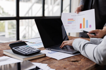 Business woman typing on laptop keyboard and financial documents, sitting at her desk in modern office, team analyzing data and preparing report