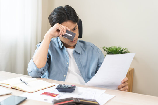Bad financial concept, frustrated asian young man having debt, reading paper report from bank, stress calculate expense from credit card invoice or bill no money to pay, mortgage or loan, bankruptcy.