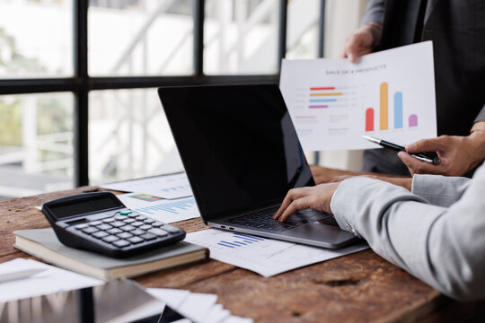 Business woman typing on laptop keyboard and financial documents, sitting at her desk in modern office, team analyzing data and preparing report