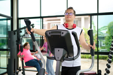 Fototapeta premium A man with down syndrome exercising on an elliptical machine in a modern gym setting with others working out in the background