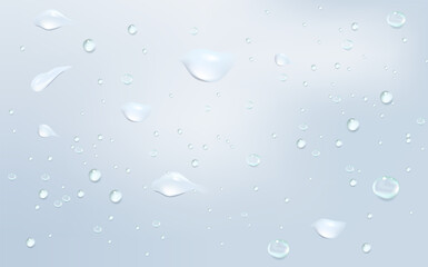 Blue transparent rain drops flowing down glass on a soft blue background.