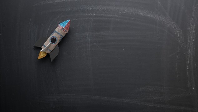 School supplies arranged with a paper rocket on a chalkboard background, flat lay from above