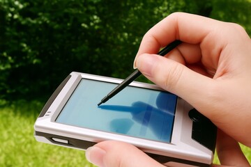 Hand using a stylus on a personal digital assistant in an outdoor setting