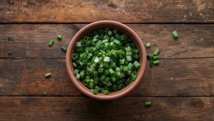 Overhead shot of a bowl filled with sliced green onions on a rustic wooden surface