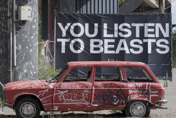 Graffiti Covered Abandoned Car in Urban Setting with Street Art and Billboard Text – Contemporary City Scene