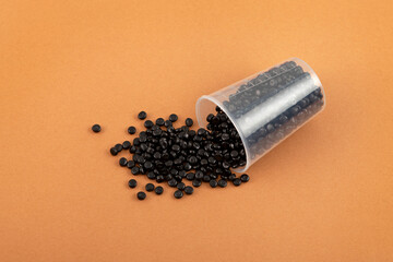Polyethylene granules scattered out of measuring cup. Uniform pellets dyed with carbon black...