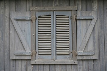 Obraz premium An old wooden window with shutters embedded in weathered planks, capturing a calm and vintage atmosphere with elegant grey and blue tones.