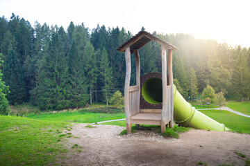 The entrance of the giant tunnel slide that descend from the hill at Pal&ugrave; Park, a huge playground located in Lavarone, Trentino, Italy. Background with copy space and sunflare.