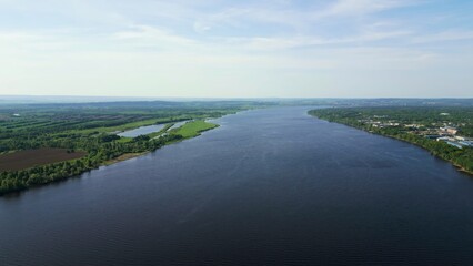 Wide river flows through green countryside under blue sky. Clip