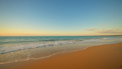 Obraz premium Morning scene at the shore with orange and yellow hues, waves shaping a sandy spit.