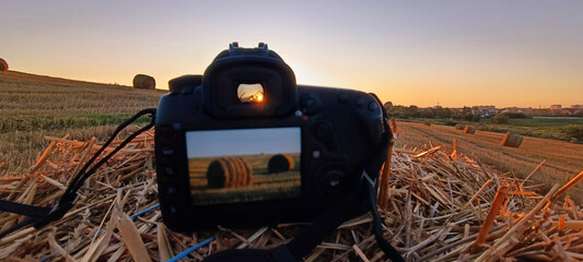DSLR camera placed on straw capturing hay bales at sunset in a golden field, symbolizing creativity, rural life, and the art of landscape photography © Photolove