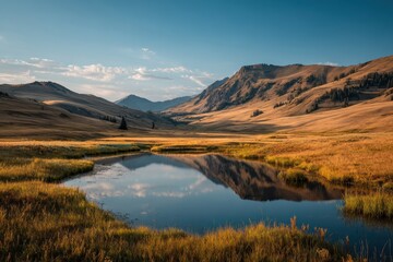 Obraz premium Golden hills reflect in the calm mountain lake under blue, partly cloudy sky. Perfect for travel, tourism, landscape, environment or outdoors concept.