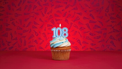 Birthday cupcake featuring number 108 candle against a vibrant red backdrop with blue flags