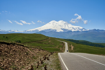 Naklejka premium Mount Elbrus in Kabardino-Balkaria, the Caucasus Republic, Russia. Snow-white peaks covered with snow and green meadows at the foot of the mountain