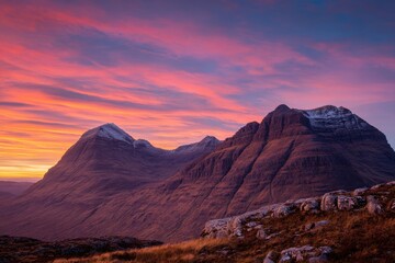 Majestic mountains under vibrant sunset sky with steep slopes and snowy patches, creating a beautiful contrast with warm tones of pink, orange, and purple against cooler rocky hues