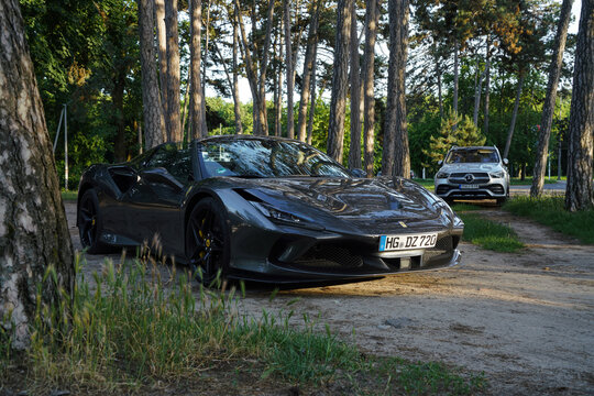 Ferrari F8 Tributo Spider supercar parked in a forest clearing, contrasting luxury high-performance vehicle with nature. Mercedes-AMG GLE in background. Palic, Serbia. May 30, 2025.
