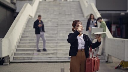 Engaged businesswoman making a friendly video call on her tablet in a busy outdoor city location. - Powered by Adobe