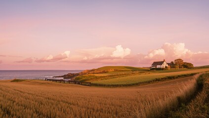 Obraz premium A breathtaking dusk painted with pink and orange shades lighting up the sky above a coastal farmstead