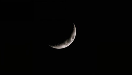 A shadowy view of the moon's hidden face with a blurred crescent moon set against a deep black sky.