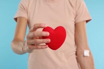 Blood donation. Woman with bandage on arm and decorative heart against light blue background,...