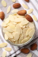 Fresh almond flakes and whole nuts in bowl on table, top view