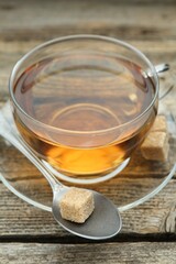 Aromatic black tea in glass cup, brown sugar and spoon on wooden table, closeup