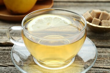 Aromatic black tea in glass cup, brown sugar and lemon on wooden table, closeup