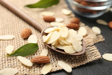Fresh almond flakes, whole nuts and green leaves on grey table, closeup