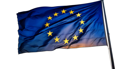 The flag of the european union, with its circle of stars, waving against a sunset white 