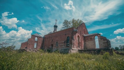 Fototapeta premium Abandoned ancient orthodox church made of red bricks under a clear blue sky and lush green grass