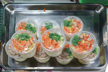 Ready-to-eat Thai mixed vegetable salad with corn, crab stick, and tuna chunks, served in a round plastic container on a metal tray. A colorful and convenient street food choice.