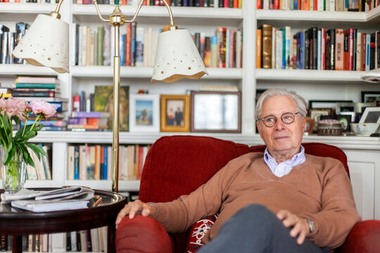 Thoughtful senior man sitting on armchair in front of bookshelf