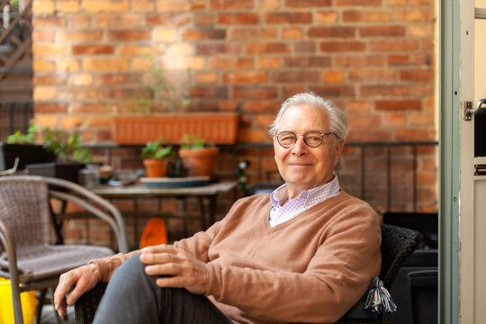 Portrait of smiling retired man sitting on chair balcony