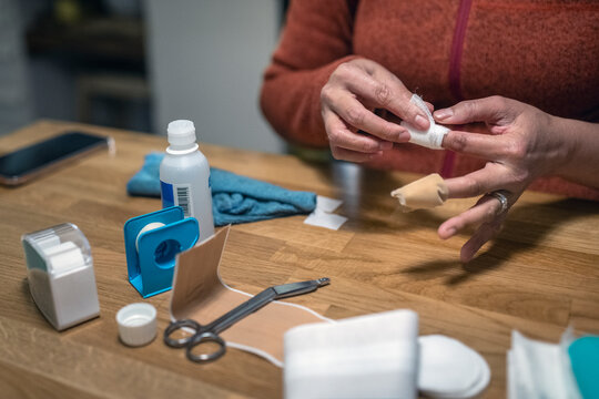 Hand of woman applying bandage on index finger at table