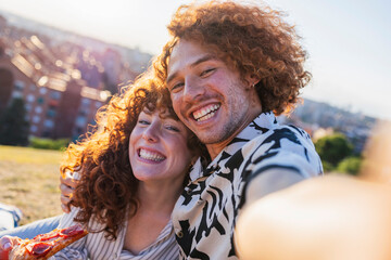 Happy couple enjoying picnic lunch taking selfie in park