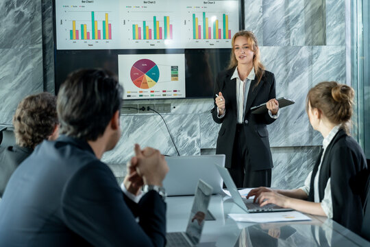 Female business presenter standing front digital board leading strategy meeting with multiracial colleagues listening analyzing financial data during team collaboration corporate session - Powered by Adobe