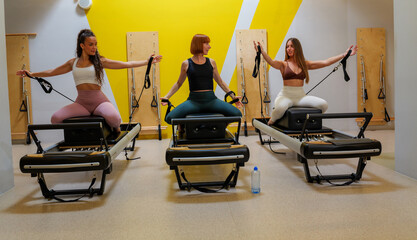 Three women performing arm exercises on pilates reformer machines, focusing on core strength and flexibility during a group workout session in a modern studio