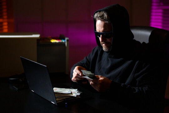 Hacker with laptop in a dark office. Anonymous hacker in a hoodie hacking data late at night. Cyber criminal and hacker stolen digital information concept. Hacker using laptop in night office.