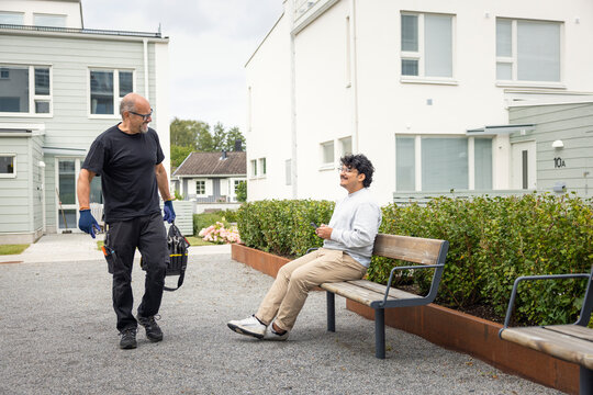 Smiling technician greeting man sitting on bench in front of building
