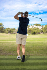 Back view of a young man playing golf at the golf course in a sunny day with blue sky.