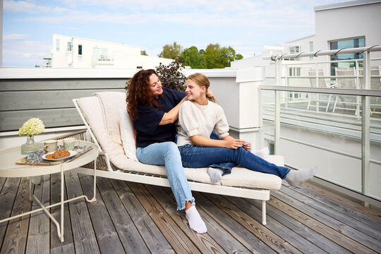 Mother talking with daughter while tying her hair sitting on lounge chair