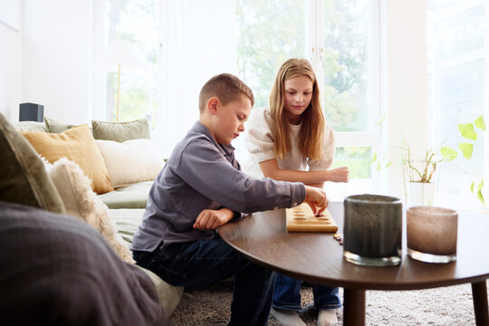 Brother and sister playing board games sitting in living room at home