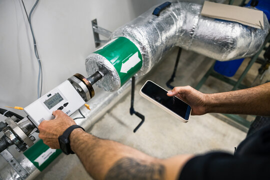 High angle view of engineer programming machine through smart phone while working at factory